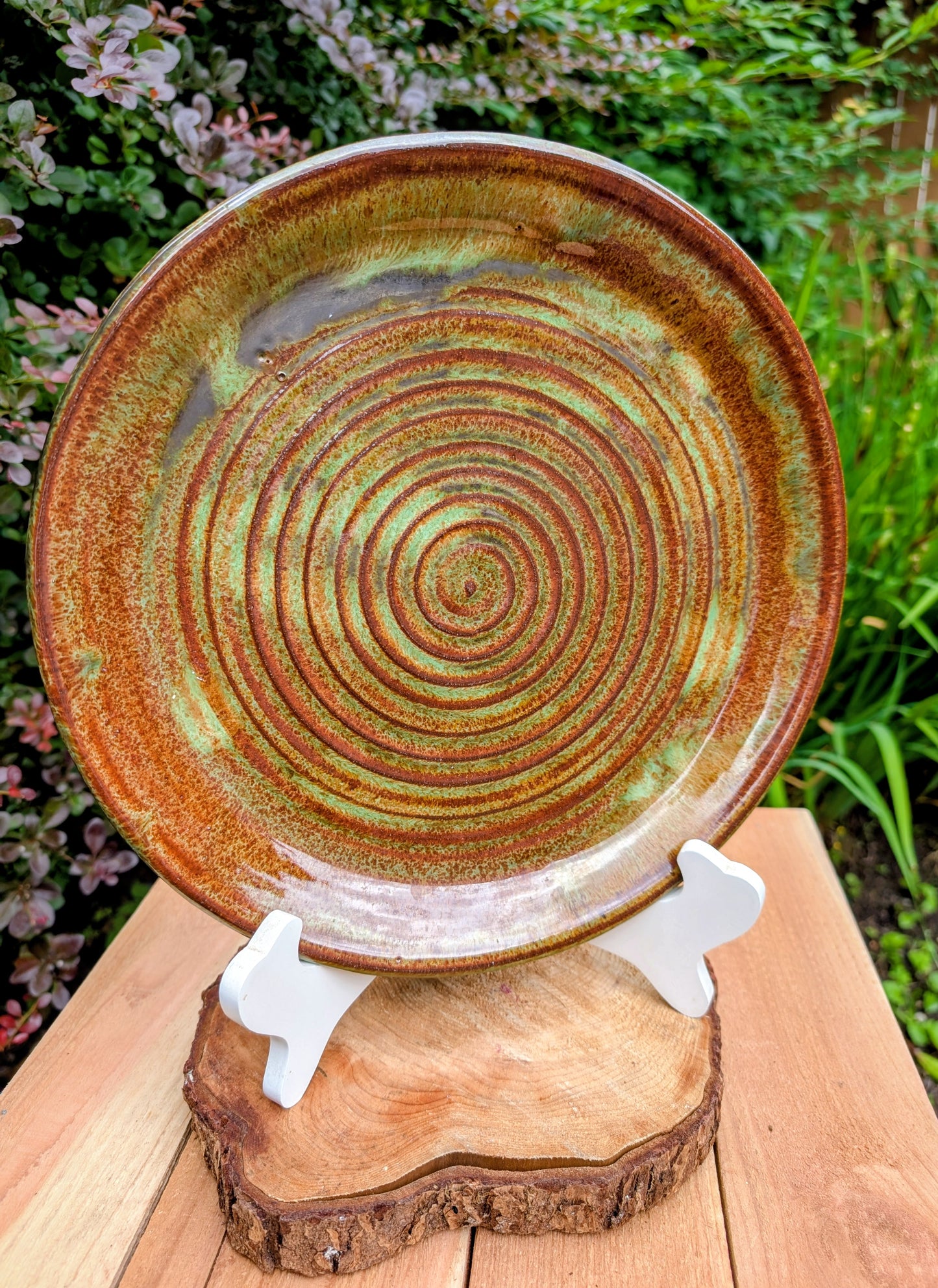 A beautifully hand-thrown studio pottery charger featuring an impressed spiral design and richly variegated moss green and rust glazes. This substantial signed stoneware piece brings timeless craftsmanship and Pacific Northwest-inspired warmth to shelves, tables, or wall displays.