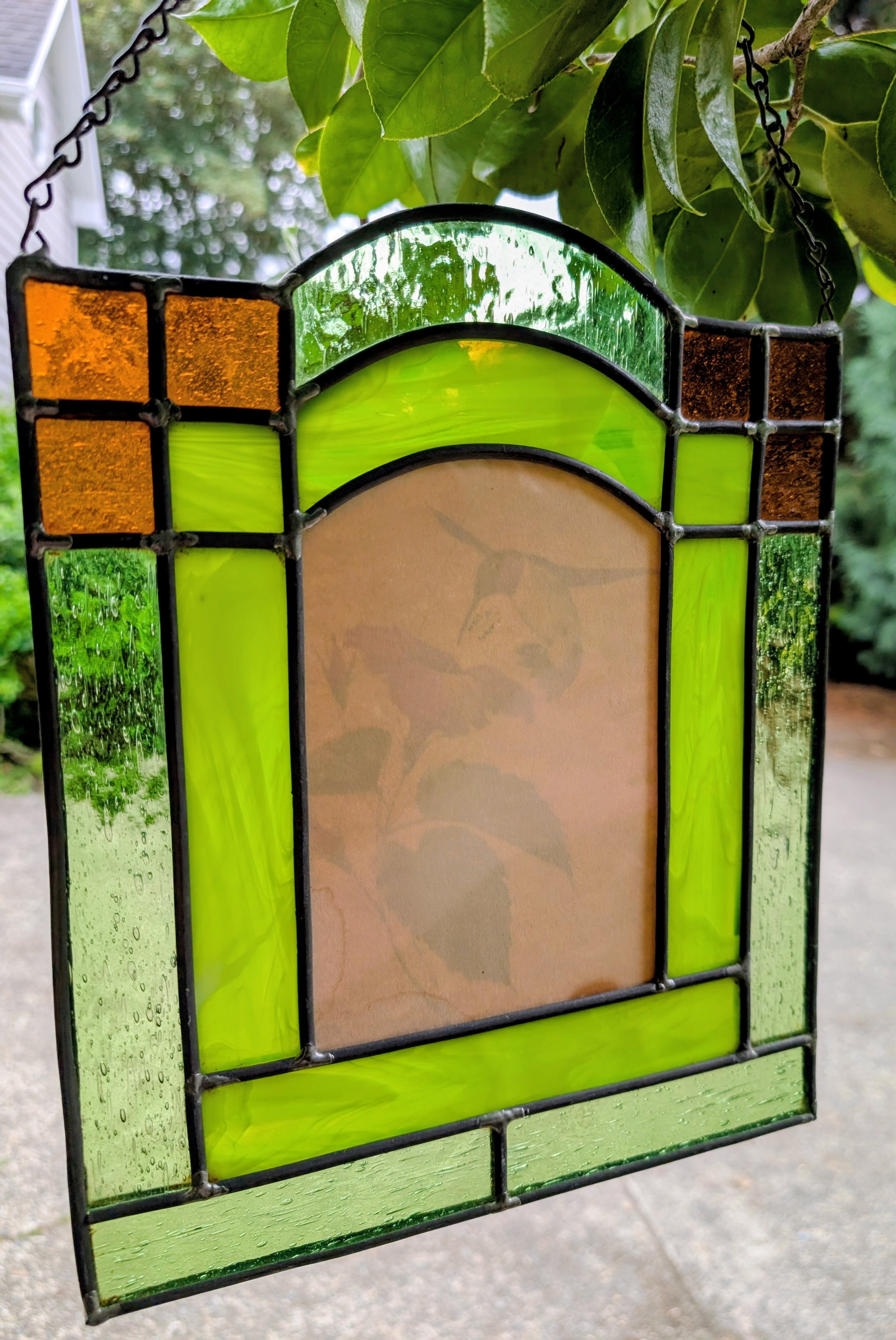 Bring the beauty of a hummingbird in bloom into your home with this handcrafted stained glass hanging panel. Featuring vibrant textured art glass surrounding a detailed hummingbird and hibiscus centerpiece, it catches natural light beautifully and adds year-round color to any window, sunroom, or garden-inspired space.