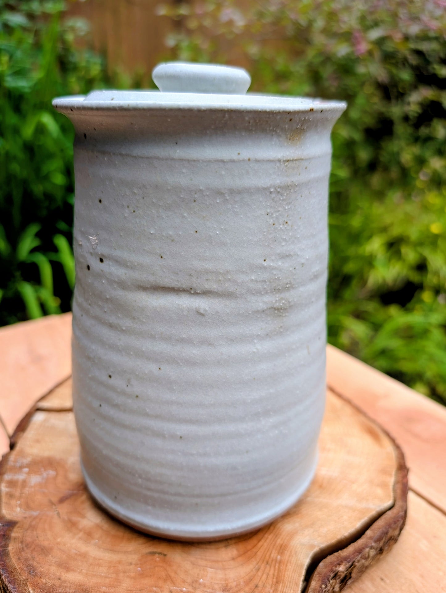 Bring warmth and handcrafted character to your kitchen with this wheel-thrown stoneware canister. Finished in a soft creamy-white glaze with subtle iron speckling, this timeless storage vessel blends rustic craftsmanship with modern organic design.