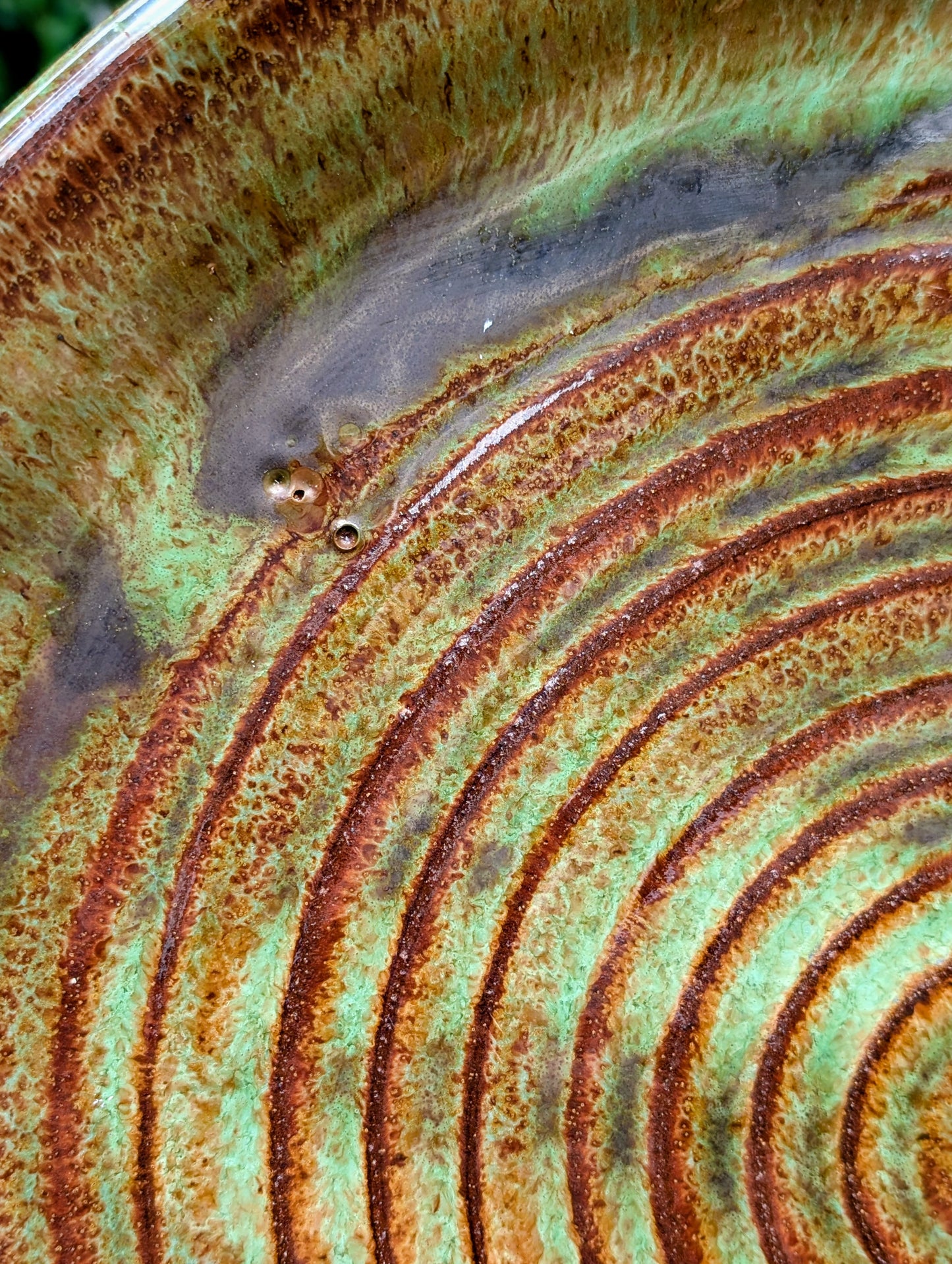A beautifully hand-thrown studio pottery charger featuring an impressed spiral design and richly variegated moss green and rust glazes. This substantial signed stoneware piece brings timeless craftsmanship and Pacific Northwest-inspired warmth to shelves, tables, or wall displays.