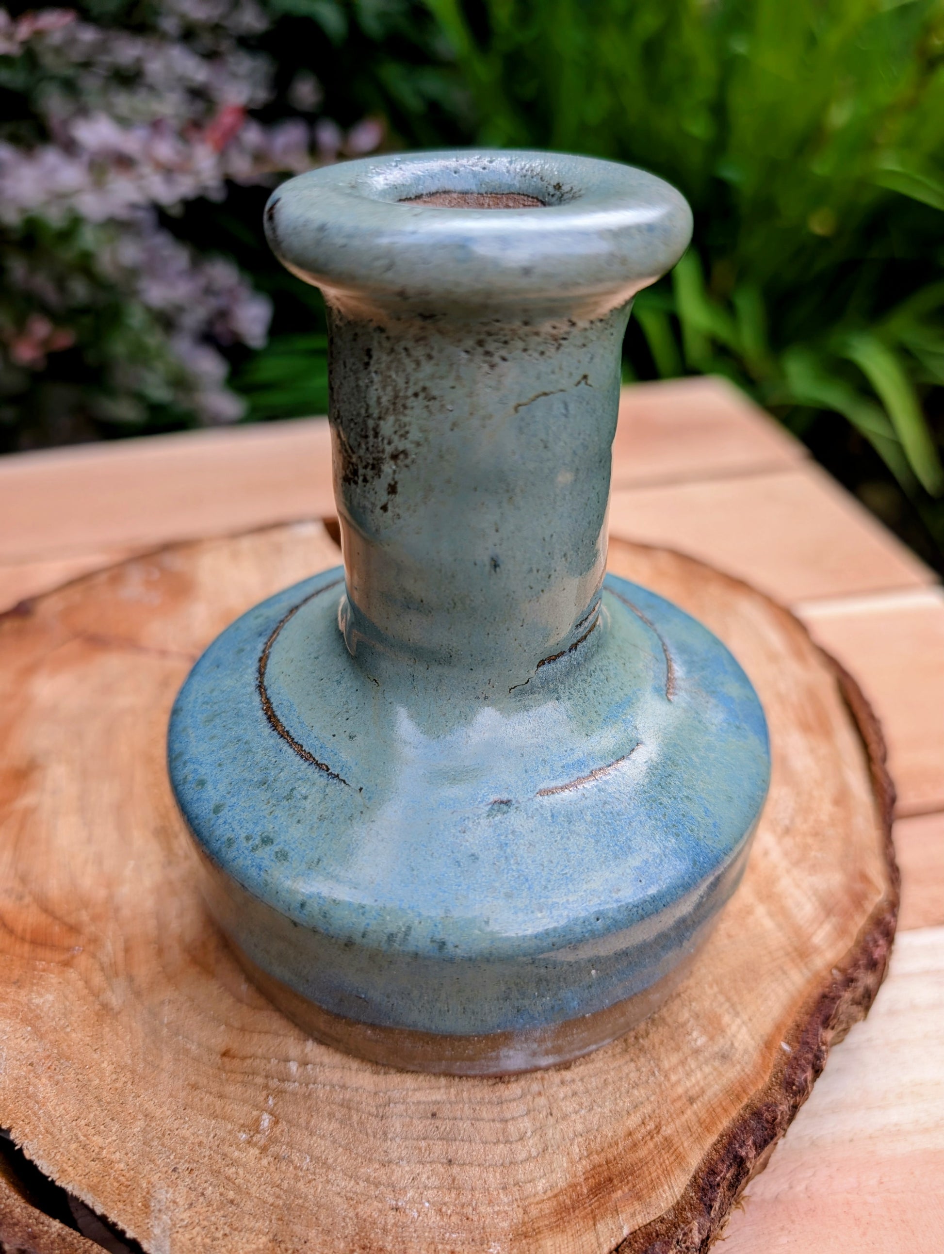 A beautifully hand-thrown studio pottery bud vase featuring a rich blue-green glaze over warm stoneware clay. Its timeless organic form makes it perfect for displaying a single bloom, dried botanicals, or as a sculptural accent in any room.