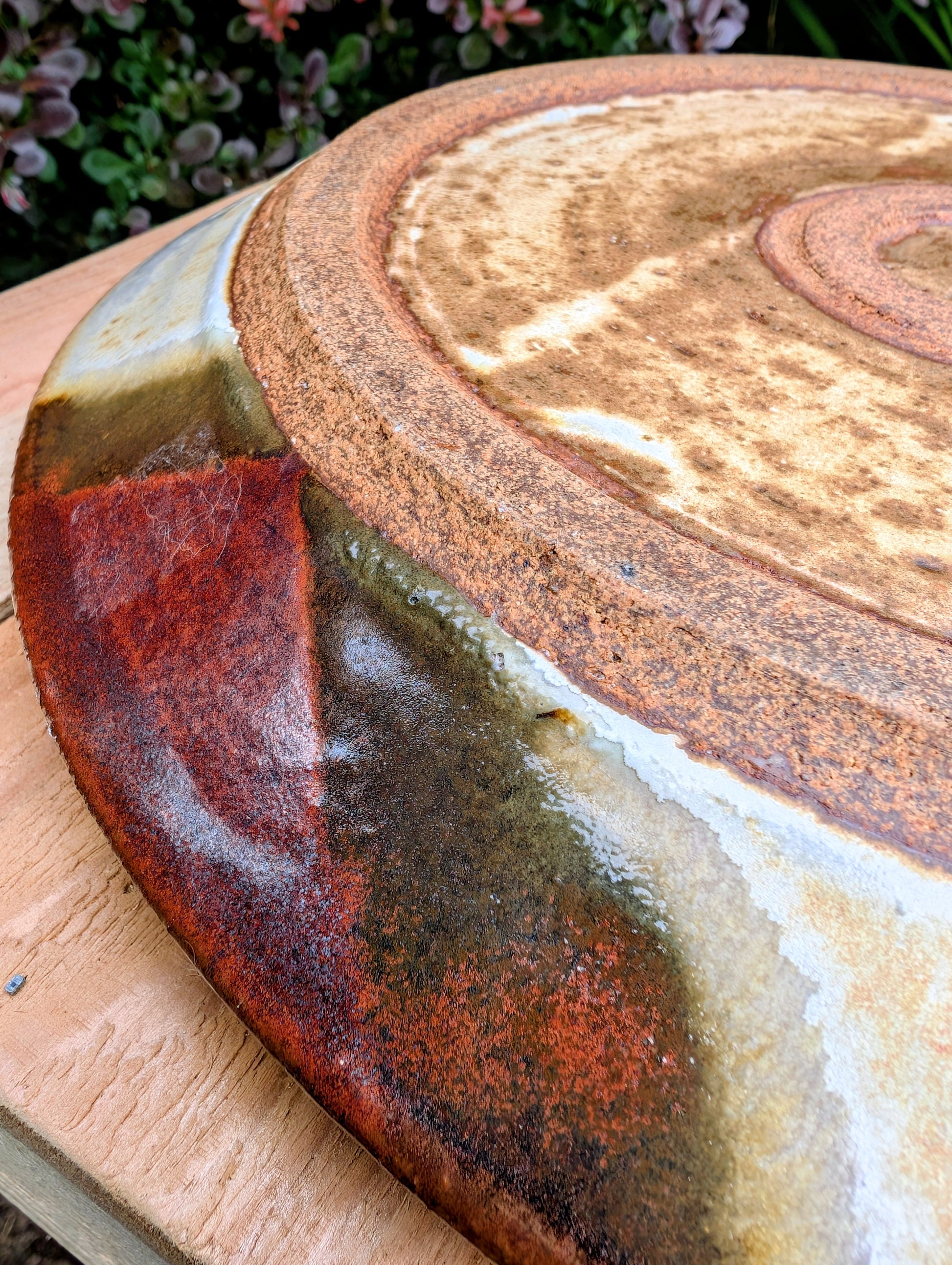 A striking hand-thrown studio pottery platter featuring an expressive cream, maroon, and olive glaze composition with visible throwing rings and an incised artist signature. Beautiful as both a decorative wall display and a functional serving piece, it embodies the warmth and craftsmanship of contemporary American studio ceramics.