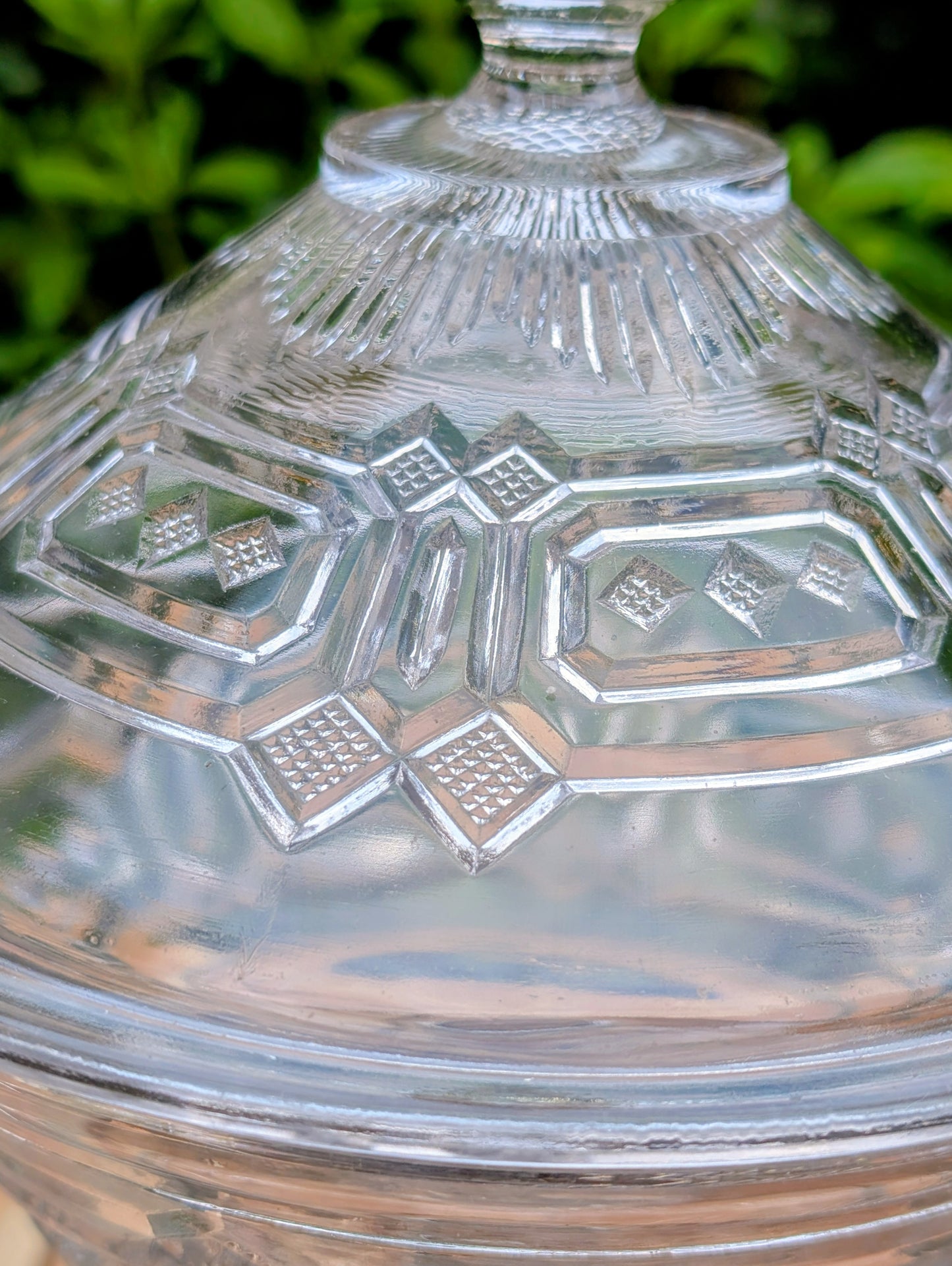An elegant early 20th-century pressed glass covered compote featuring bold geometric Art Deco styling and a striking pedestal silhouette. Although the pedestal has visible stress cracks, the original lid, impressive scale, and architectural design make it a beautiful decorative display piece.