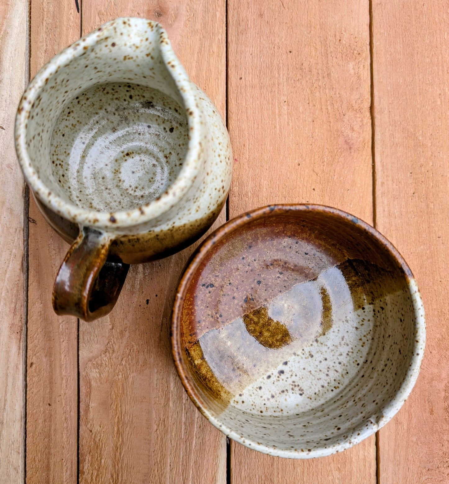 Bring handcrafted warmth to your table with this signed studio pottery creamer and sugar bowl set. Finished in a beautiful speckled cream glaze with flowing olive-brown accents, this artisan stoneware pair blends rustic craftsmanship with timeless everyday function.