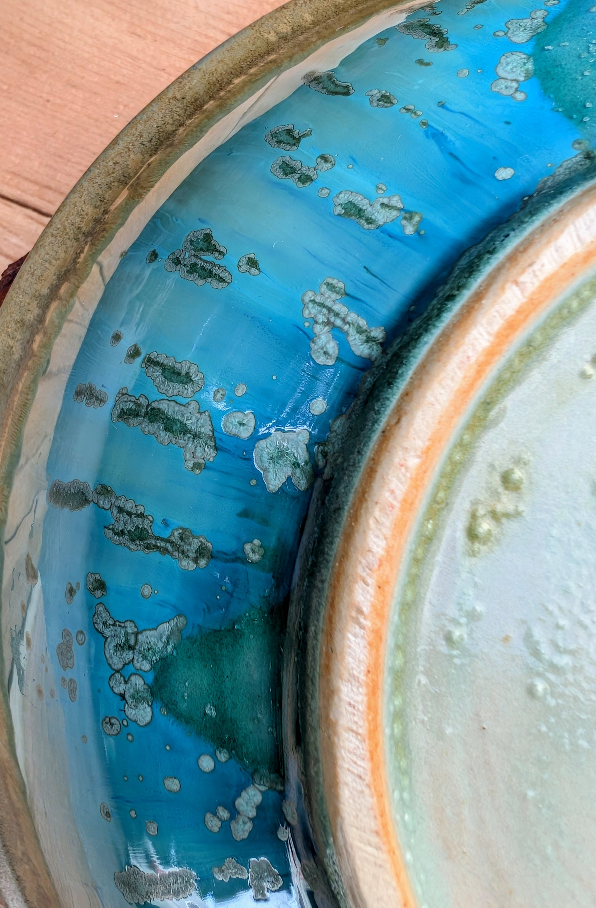 A beautifully handcrafted studio pottery bowl featuring layered blue, celadon, and copper reactive glazes with striking crystalline patterning. This artisan stoneware piece makes an eye-catching centerpiece or decorative accent inspired by the colors of Pacific Northwest waters.
