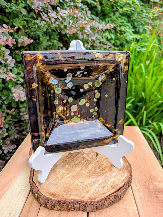 Bring handcrafted artistry into your home with this one-of-a-kind square studio pottery dish. Its rich chocolate brown glaze is accented by constellation-like blue, green, and cream crystalline details, making it equally beautiful as a decorative catchall, appetizer dish, or display piece.