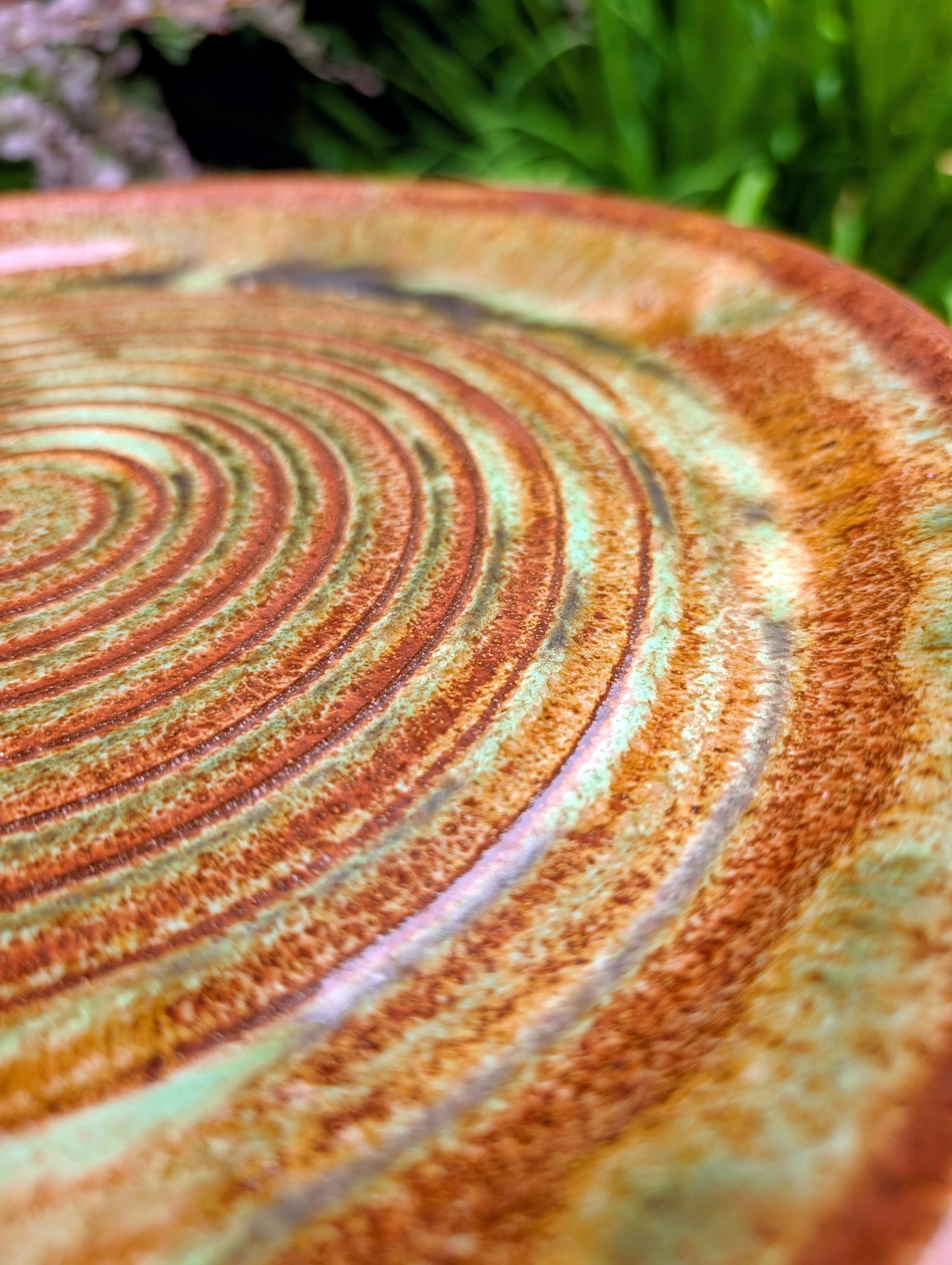 A beautifully hand-thrown studio pottery charger featuring an impressed spiral design and richly variegated moss green and rust glazes. This substantial signed stoneware piece brings timeless craftsmanship and Pacific Northwest-inspired warmth to shelves, tables, or wall displays.
