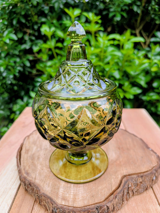 Bring timeless Mid-Century elegance to your home with this authentic Fostoria Argus covered pedestal compote in rich olive green glass. Crafted in the early 1960s, its bold geometric design and substantial weight make it a beautiful display piece for every season.